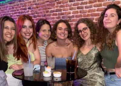 Grupo de seis amigas menores de 30 años sentadas miran y sonríen felices a cámara